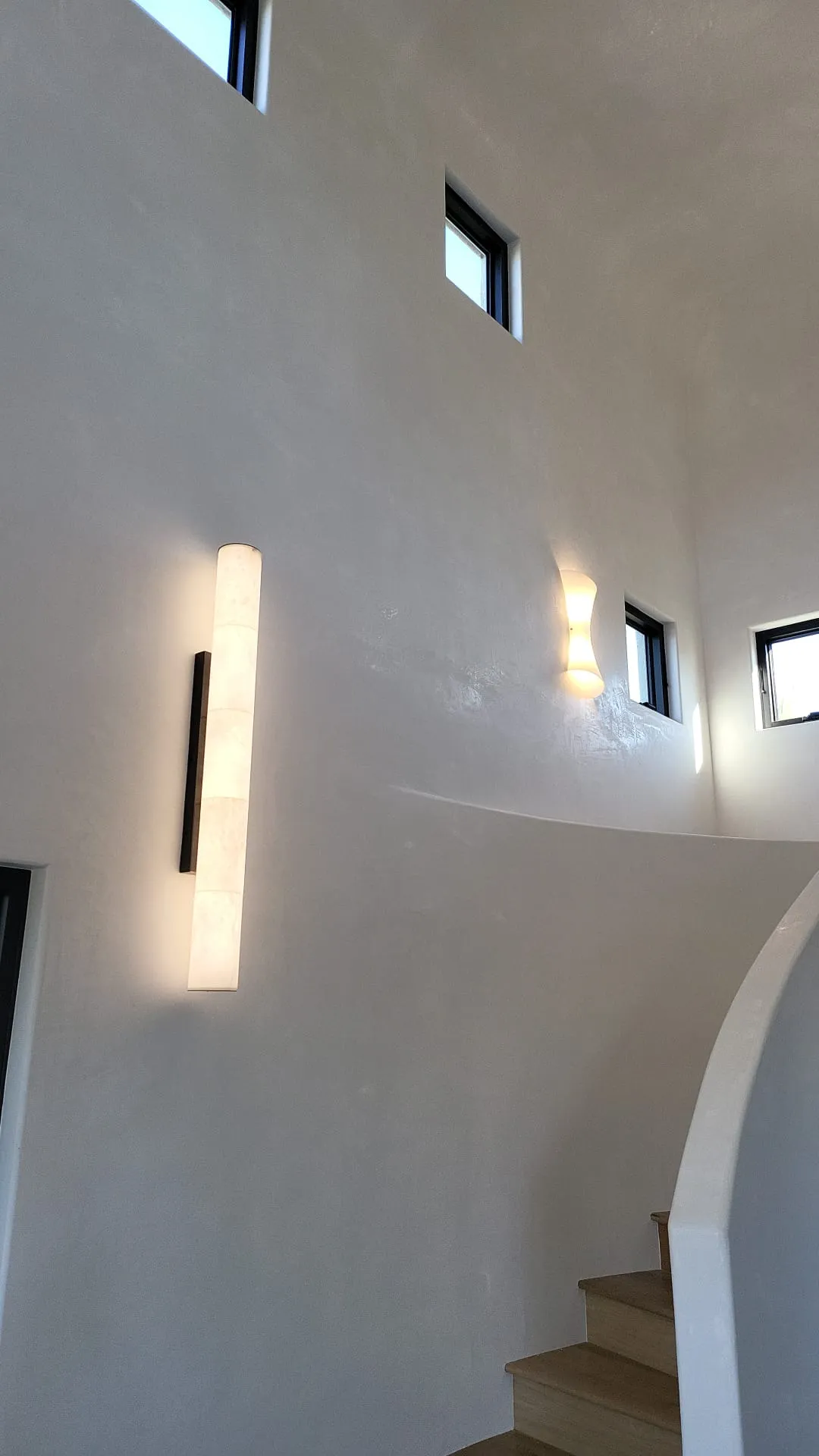 Stucco entryway with curved walls, vertical alabaster sconce and pendant. Architectural lighting by Martinez Electric Corp