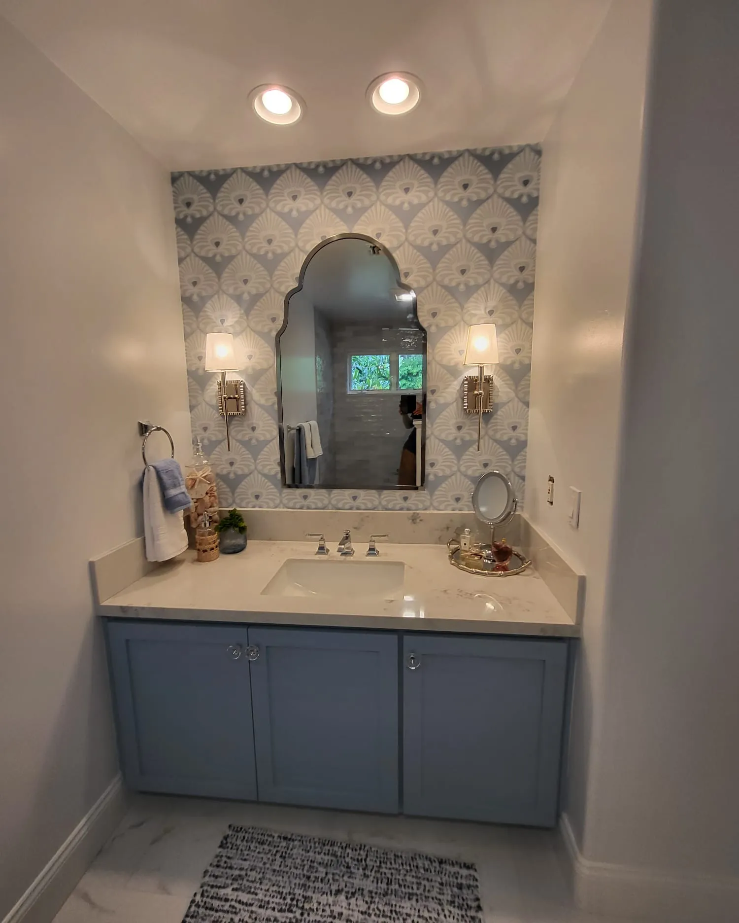 Powder bath with arched mirror, blue cabinets and decorative wallpaper. Sconces + recessed lights installed by Martinez Electric Corp