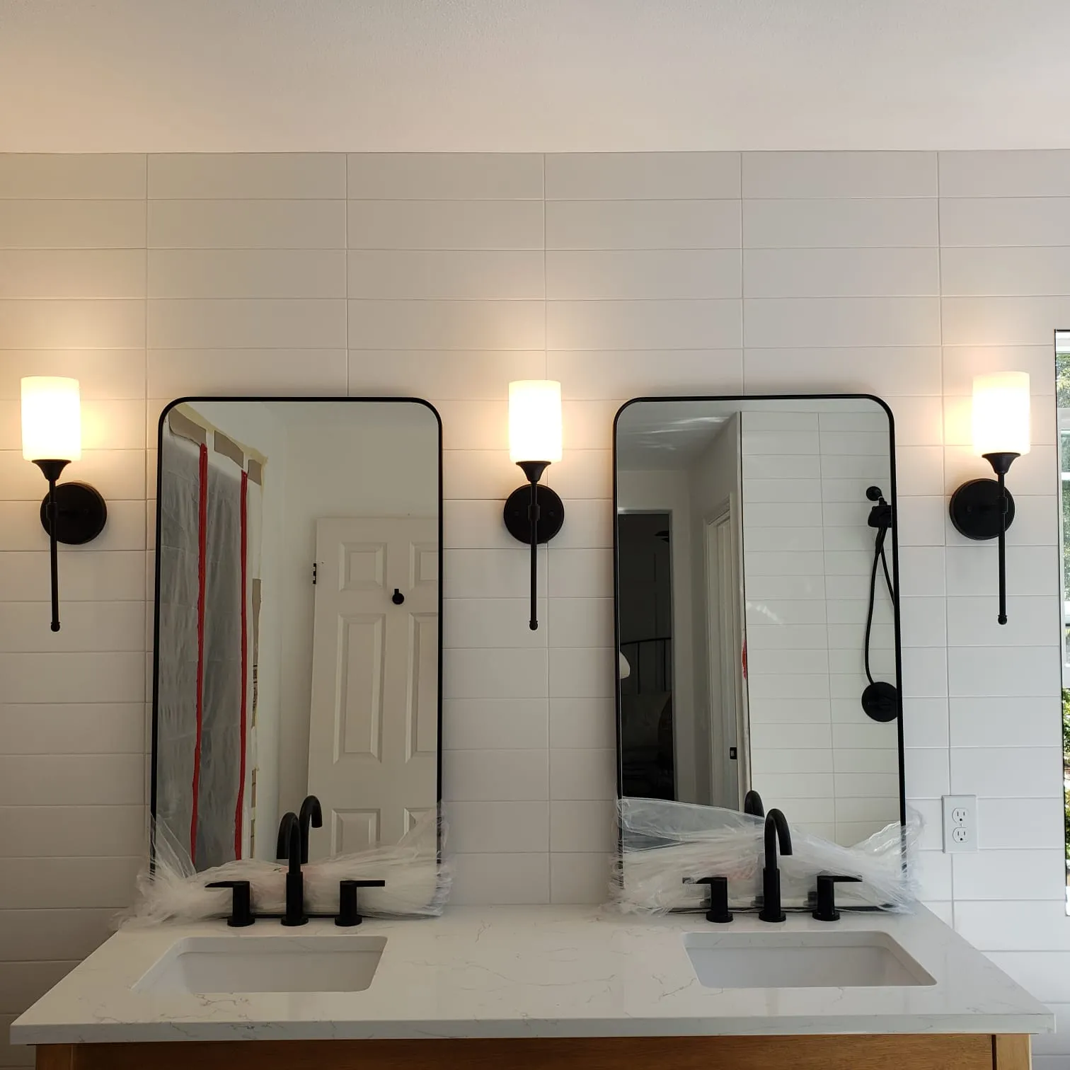 Black-base glass-globe sconces flanking double mirrors over marble vanity. Martinez Electric Corp