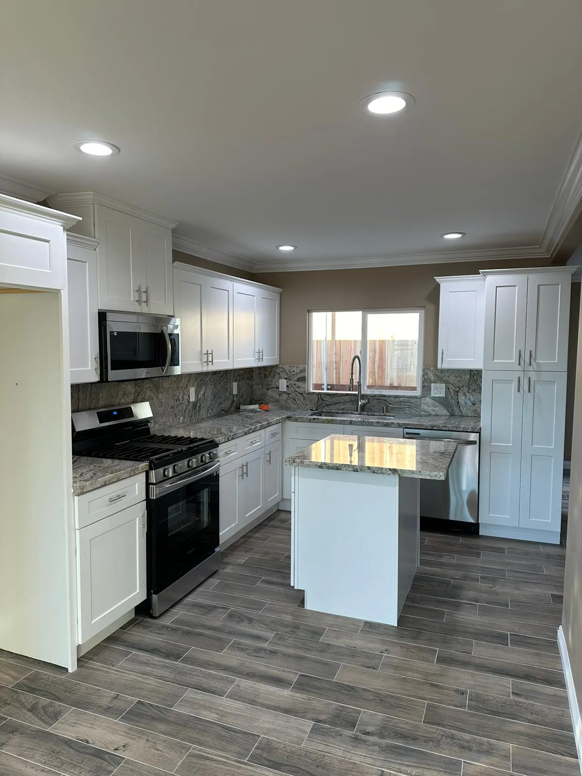 White kitchen with granite island, shaker cabinets and recessed lighting. Martinez Electric Corp