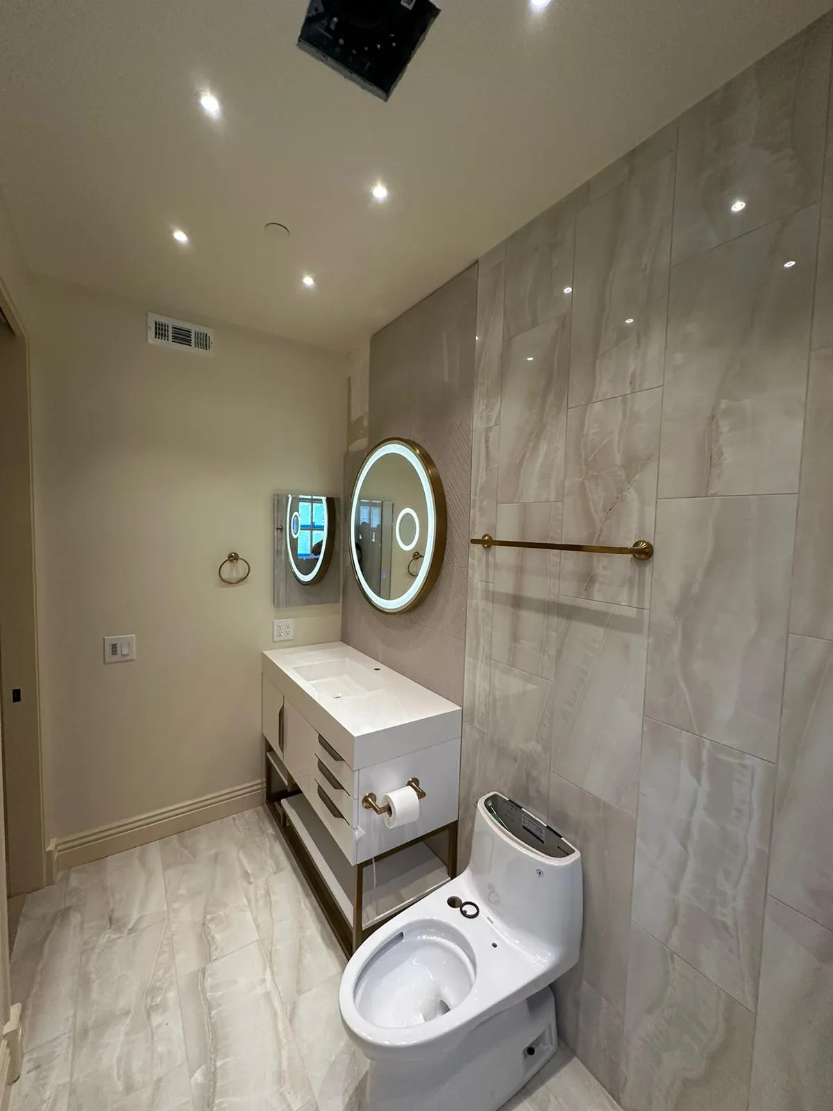 Modern bathroom with backlit round mirror, brass fixtures and marble tile. Martinez Electric Corp