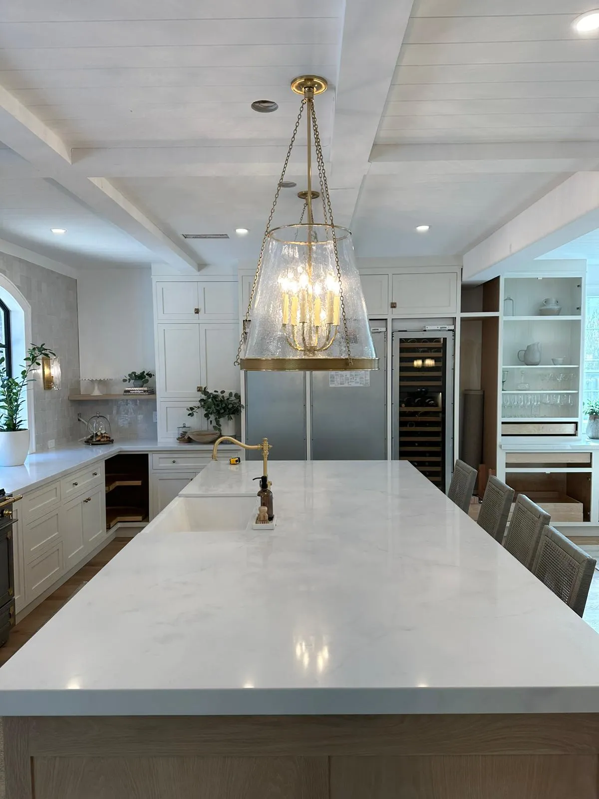 Modern kitchen with brass chandelier over marble island and integrated wine fridge. Martinez Electric Corp