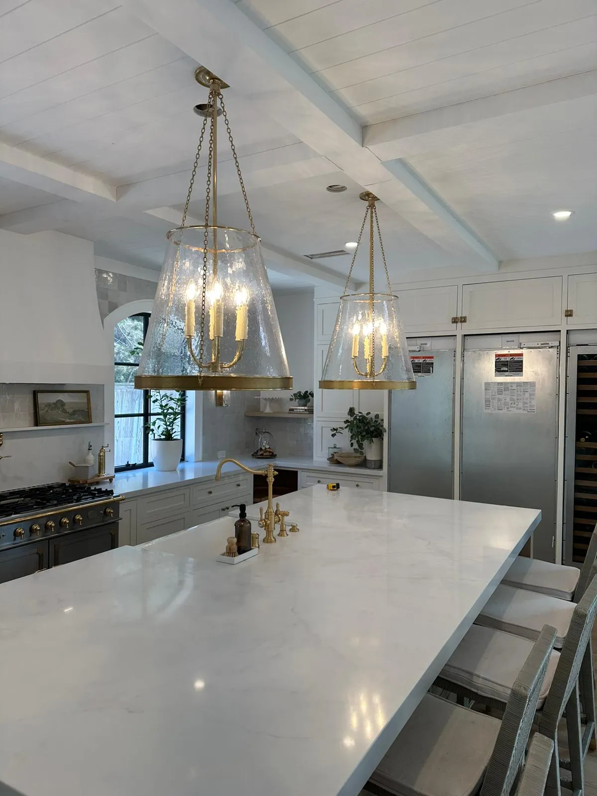 Spanish-style kitchen with brass + glass pendants over marble island and pro range with brass accents. Martinez Electric Corp